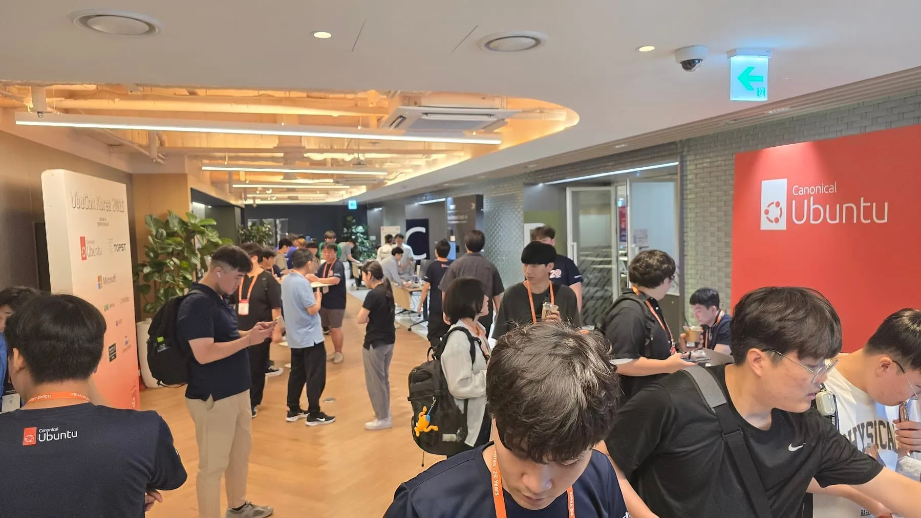 많은 사람들이 행사장 안을 거닐고 있습니다. 왼쪽으로는 UbuCon Korea 2025 라고 적힌 포토월이, 오른쪽으로는 Canonical Ubuntu 부스가 보입니다.